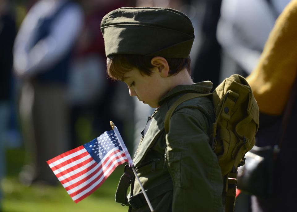 Five-year-old Haomhan Wing bows his head during the benediction wearing a military jumpsuit with his grandfather's ID patch on it on the Hyannis Town Green as part of the town's 2021 Veterans Day observance.