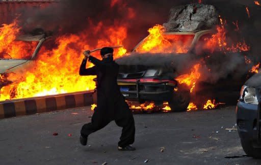 A Pakistani Muslim demonstrator brandishes a stick near burning police vehicles during a protest against an anti-Islam film in Karachi