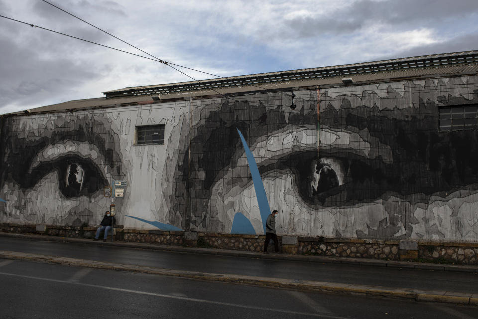 Two men wearing face masks to prevent the spread of the coronavirus walk past a giant mural by Greek street artist iNO depicting the eyes of Leonardo da Vinci's Mona Lisa, in Athens, Thursday, Dec. 10, 2020. Greece is expected to see a 10.5% contraction of its gross domestic product this year, above the forecasted EU average of 7.4%, while its debt-to-GDP ratio is set to surge to a staggering 208.9% according to the EU and Greek authorities. (AP Photo/Petros Giannakouris)
