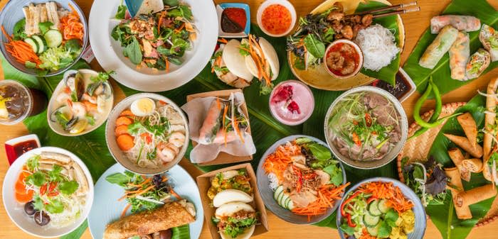 A large assortment of delicious and brightly colored Vietnamese dishes are spread on a table