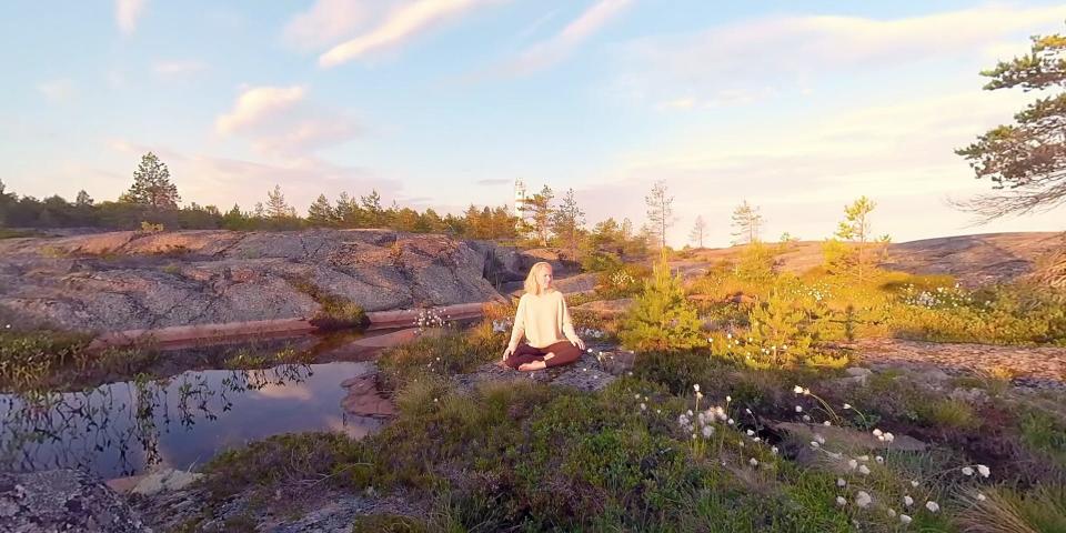 A woman sits in a rocky, wet field in a sunset cross-legged.