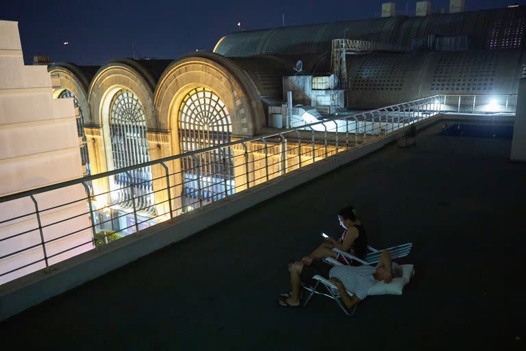 El encargado, Carlos Arévalo duerme en la terraza porque no soporta el calor; enfrente el centro comercial desborda de iluminación