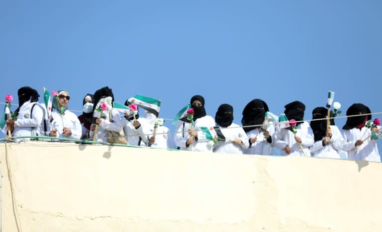 Syrian health workers hold opposition flags and roses as in the village of Atme in northern Idlib province on September 16, 2018