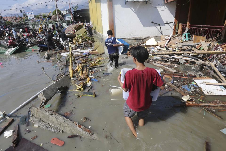 People carry items from a shopping mall badly damaged by a massive earthquake and tsunami in Palu, Central Sulawesi, Indonesia, Sunday, Sept. 30, 2018. Rescuers were scrambling Sunday to try to find trapped victims in collapsed buildings where voices could be heard screaming for help after a massive earthquake in Indonesia spawned a deadly tsunami two days ago. (AP Photo/Tatan Syuflana)