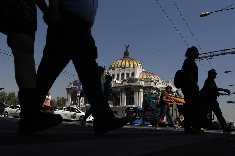 People walk past the Palace of Fine Arts in downtown Mexico City, where car and pedestrian traffic is visibly reduced over coronavirus concerns, Tuesday, March 24, 2020. Beginning Monday, Mexico's capital shut down museums, bars, gyms, churches, theaters, and other non-essential businesses that gather large numbers of people, in an attempt to slow the spread of the new coronavirus that causes Covid-19. (AP Photo/Rebecca Blackwell)