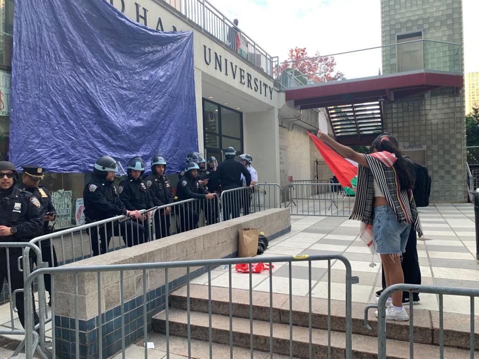 About a dozen police officers stand on one side of a barricade at Fordham University. Two protesters stand facing them on the other side of the barricade.
