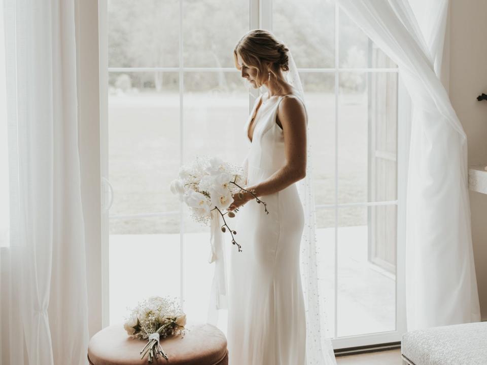 A bride standing in front of a window holding a bouquet.