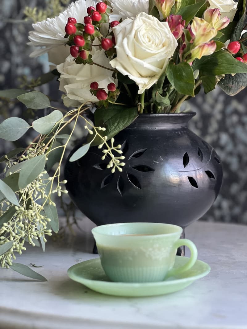 Black vase of flowers and jade coffee cup with saucer