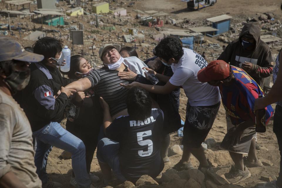 Relatives comfort a family member during the burial service of 85-year-old Lupicino Fernandez who died from the new coronavirus, at the Nueva Esperanza cemetery on the outskirts of Lima, Peru, Wednesday, May 27, 2020. (AP Photo/Rodrigo Abd)