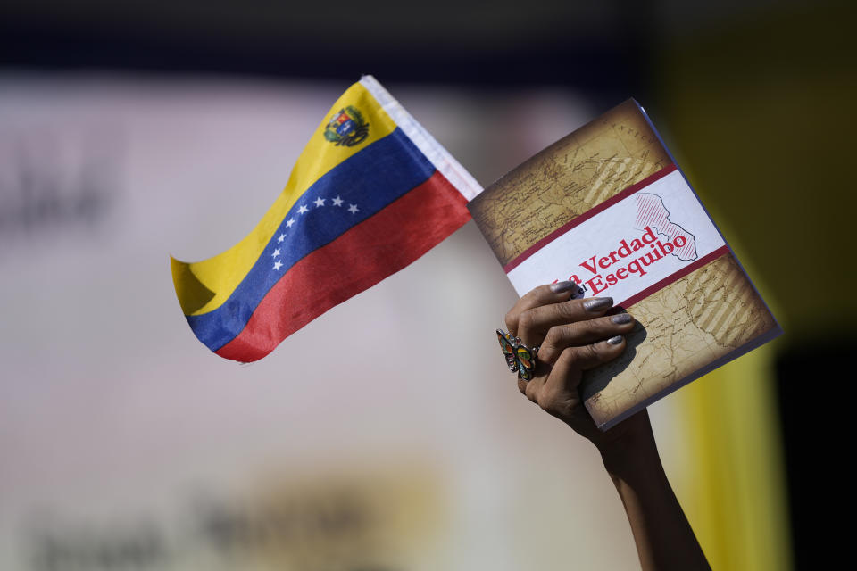 Una mujer sostiene una bandera venezolana y un libro sobre la disputa del territorio de Esequibo en Caracas, el miércoles 29 de noviembre de 2023. (AP Foto/Matias Delacroix)