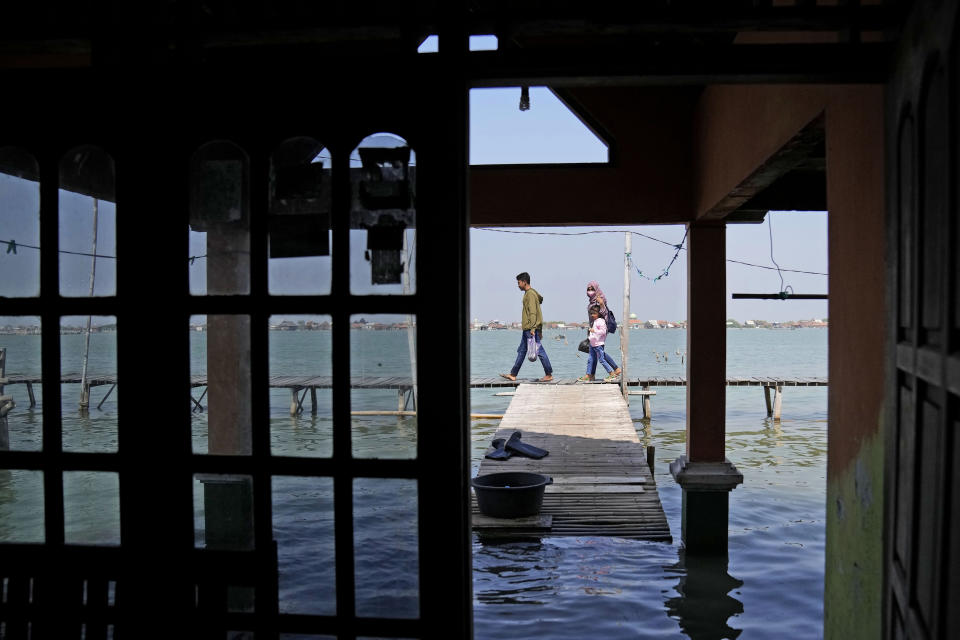 Una familia camina por un pequeño muelle junto a una casa inundada en Timbulsloko (Java, Indonesia) el 31 de julio del 2022. (AP Photo/Dita Alangkara)