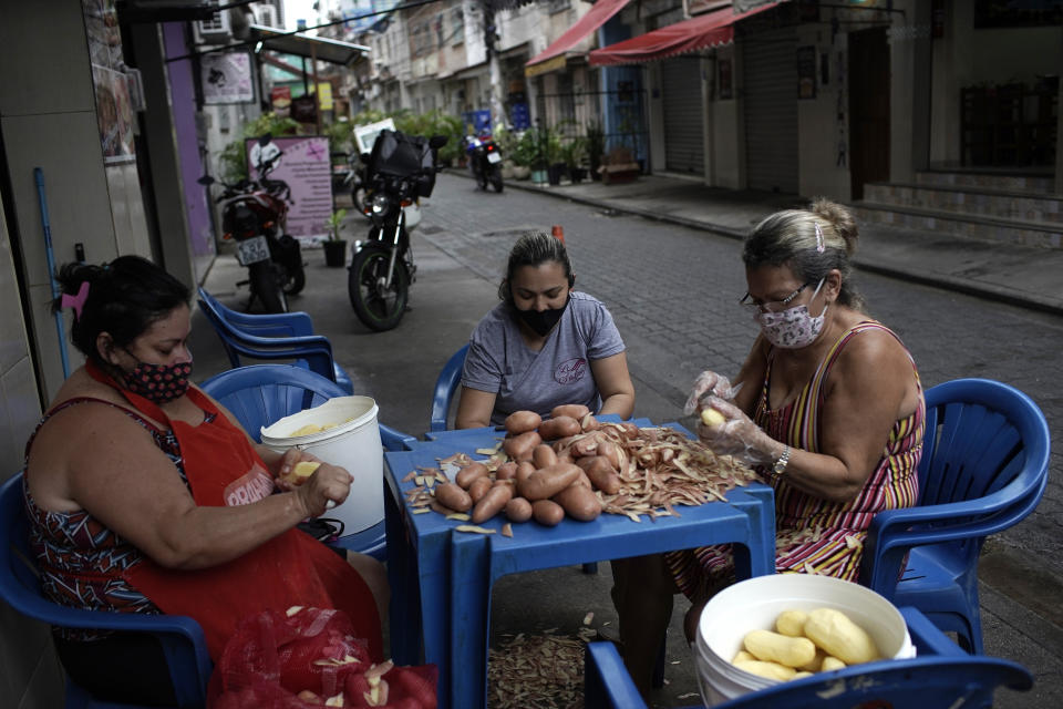 Women peel potatoes outside a snack bar amid the new coronavirus pandemic in Rio de Janeiro, Brazil, Friday, Oct. 9, 2020. Many people in Brazil are struggling to cope with less pandemic aid from the government and jumping food prices, with millions expected to slip back into poverty. (AP Photo/Silvia Izquierdo)