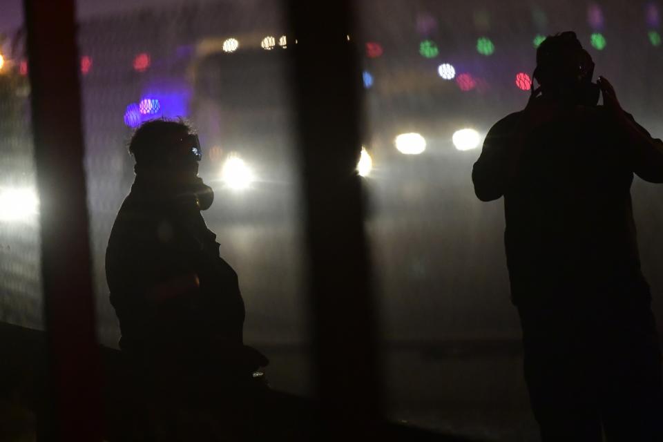 People stand behind a fence of a highway during a wildfire in Afidnes area, northern Athens, Greece, Thursday, Aug. 5, 2021. Wildfires rekindled outside Athens and forced more evacuations around southern Greece Thursday as weather conditions worsened and firefighters in a round-the-clock battle stopped the flames just outside the birthplace of the ancient Olympics. (AP Photo/Michael Varaklas)