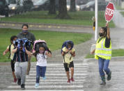 A crossing guard stops traffic for elementary school children to make their way across the street after school let out during a rain storm in Richardson, Texas, Wednesday, Sept. 9, 2020. Many schools across Texas resumed face to face classes this week. (AP Photo/LM Otero)