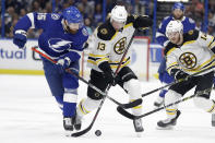 Boston Bruins center Charlie Coyle (13) and Tampa Bay Lightning defenseman Braydon Coburn (55) battle for the puck during the first period of an NHL hockey game Tuesday, March 3, 2020, in Tampa, Fla. Trailing the play is Bruins right wing Chris Wagner (14). (AP Photo/Chris O'Meara)
