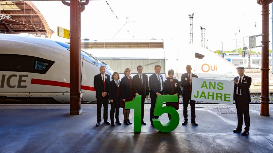 People gathered at a terminal celebrating the partnership between DB and SNCF. The row pf people are holding a banner and a cutout of the number 15.