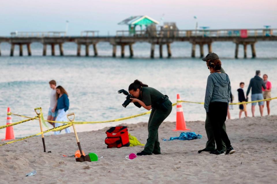 Investigadores en la playa de Lauderdale-by-the-Sea toman fotos del hueco en la arena donde el martes, 20 de febrero de 2024, una niña de siete años murió después que colpasó la arena del agujero que estaba haciendo con su hermano.
