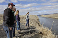 In this March 2, 2020, hoto, farmer Ben DuVal; his wife, Erika, and their daughters, Hannah, 12, in purple, and Helena, 10, in gray, stand near a canal for collecting run-off water near their property in Tulelake, Calif. Ben DuVal inherited the farm from his grandfather, a World War II veteran who won the land by lottery, and worries that plan to demolish four dams on the lower Klamath River could set a precedent for dam removal that could eventually threaten his livelihood. The proposal to remove the dams on California's second-largest river to benefit threatened salmon has sharpened a decades-old dispute over who has the biggest claim to the river's life-giving waters. (AP Photo/Gillian Flaccus)