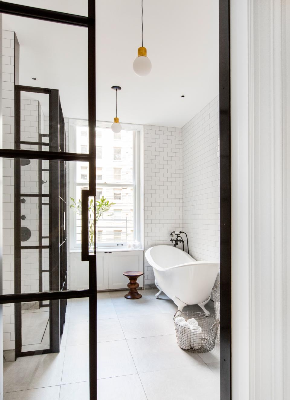 The master bathroom—one of six bathrooms in the apartment—features iron-framed glass divisions designed by Grehl. “We wanted very minimal, clean details that wouldn’t take away from the existing architecture,” she says. To balance the sharp lines and masculinity of the metalwork, the designer chose a curvy claw-foot tub from Chevriot. The Eames walnut stool is from Design Within Reach.