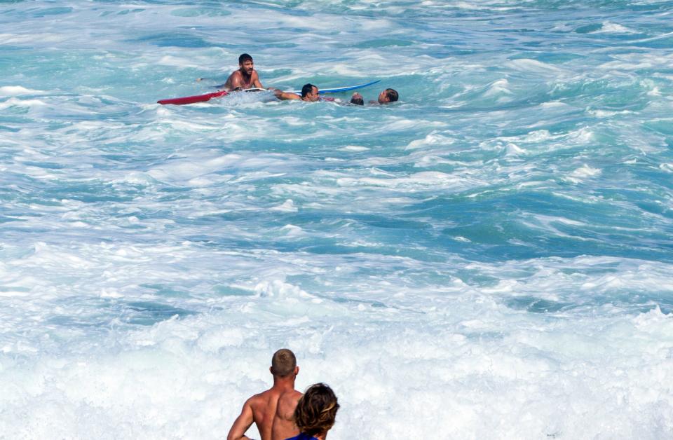 Bodyboarder Andre Botha, top left, watches as two lifeguards help him rescue pro surfer Evan Geiselman, second from right, as surfer Mick Fanning, bottom center, runs toward the ocean at the North Shore Oahu surfing spot known as Pipeline, near Haleiwa, Hawaii, on Dec. 6.