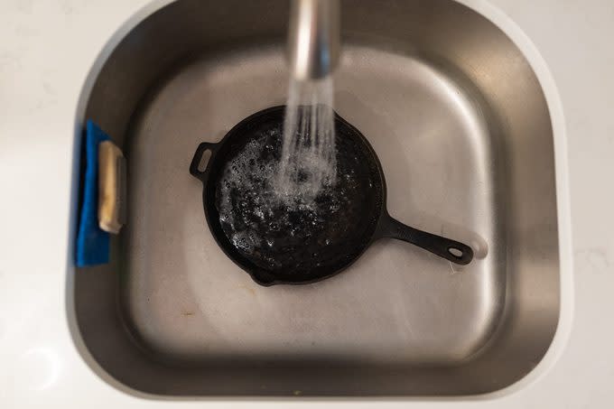 cast iron skillet in sink being rinsed with water