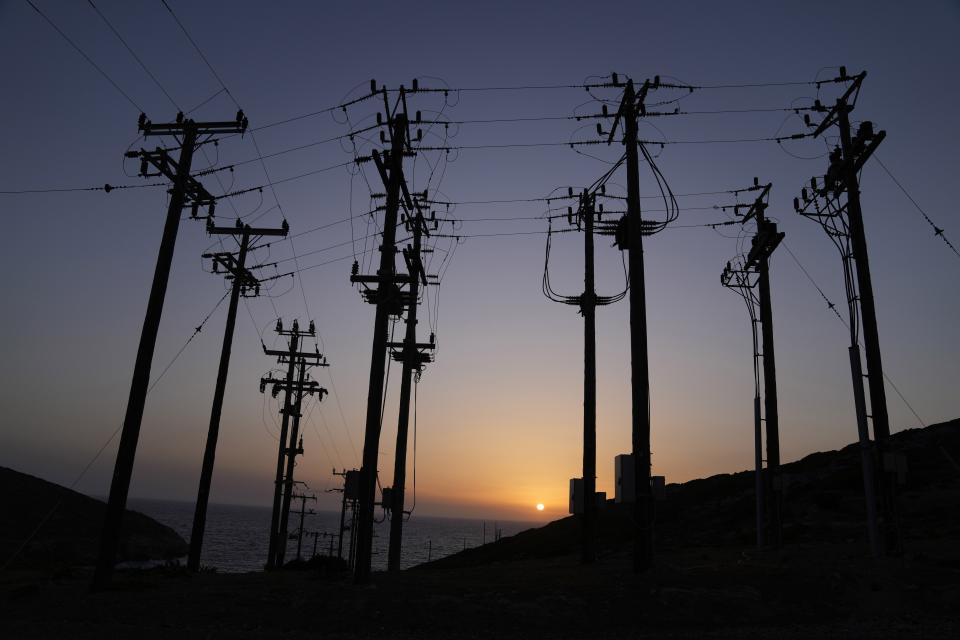 The sun sets behind electricity posts on the Aegean Sea island of Tilos, southeastern Greece, Monday, May 9, 2022. When deciding where to test green tech, Greek policymakers picked the remotest point on the map, tiny Tilos. Providing electricity and basic services, and even access by ferry is all a challenge for this island of just 500 year-round inhabitants. It's latest mission: Dealing with plastic. (AP Photo/Thanassis Stavrakis)