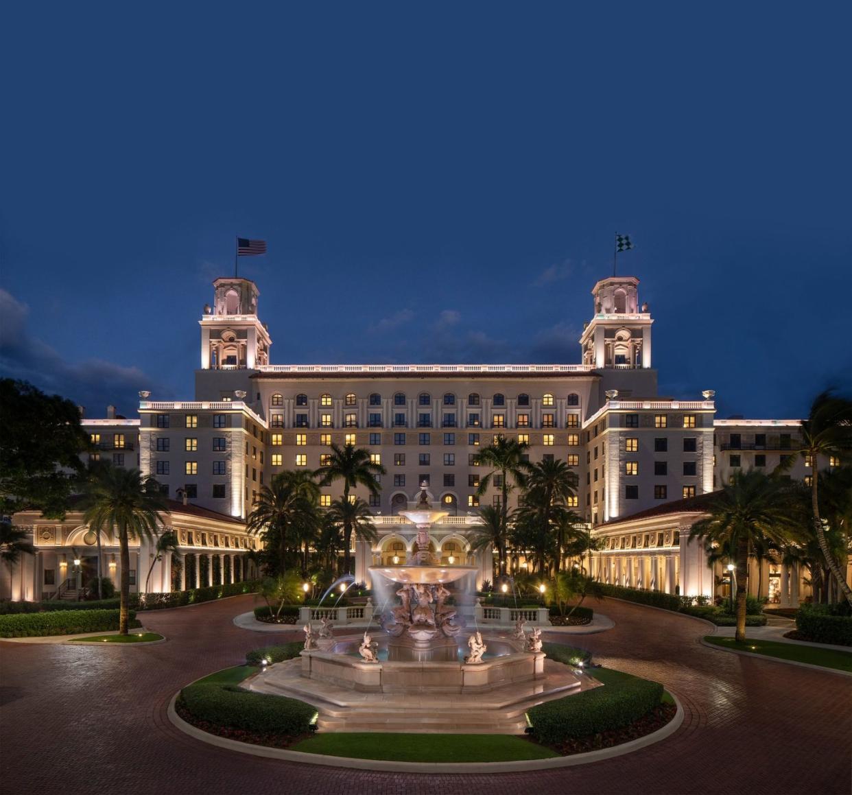 a large building with a fountain and palm trees in front of it