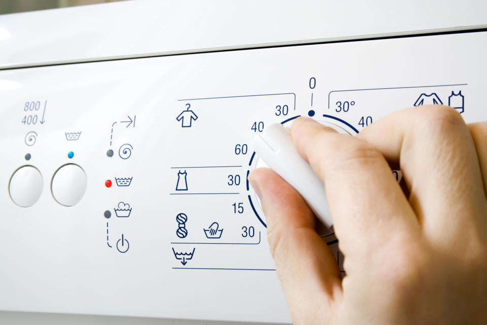 A hand turns up the temperature knob on a washing machine to 40C