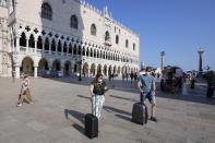 Tourists walk with luggage across St. Mark's square, in Venice, Italy, Thursday, June 17, 2021. After a 15-month pause in mass international travel, Venetians are contemplating how to welcome visitors back to the picture-postcard canals and Byzantine backdrops without suffering the indignities of crowds clogging its narrow alleyways, day-trippers perched on stoops to imbibe a panino and hordes of selfie-takers straining for a spot on the Rialto Bridge or in front of St. Mark’s Basilica. (AP Photo/Luca Bruno)