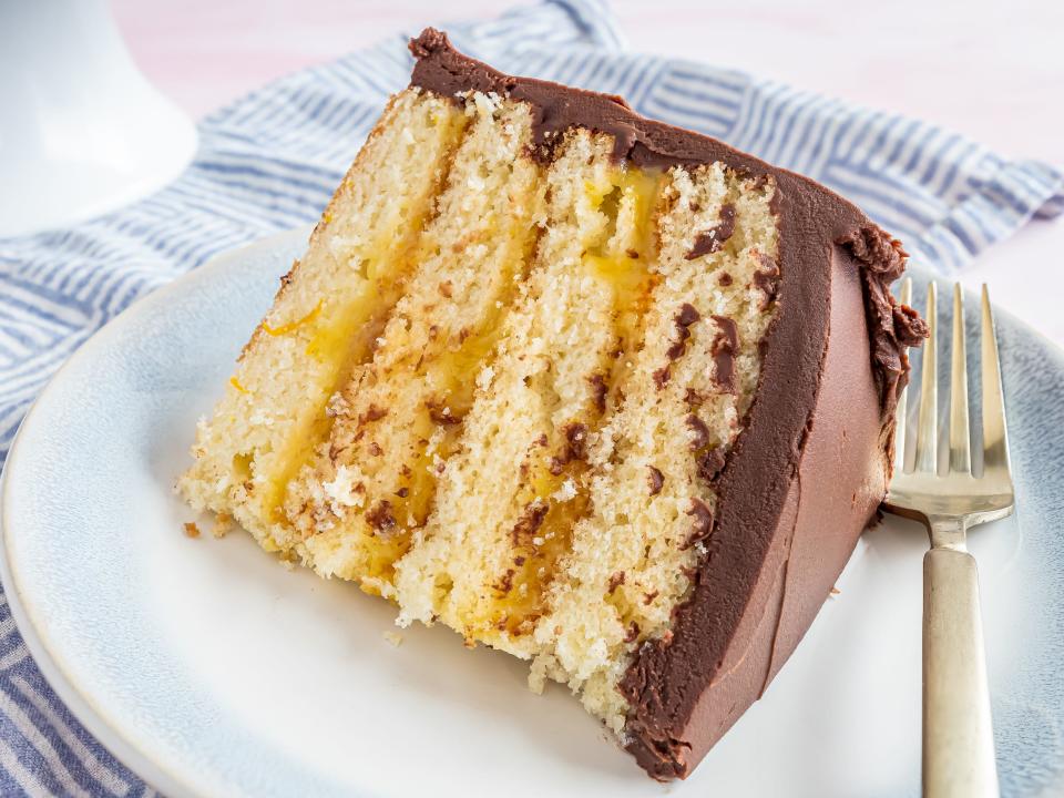 a slice of yellow cake with orange filling covered in chocolate frosting with a fork