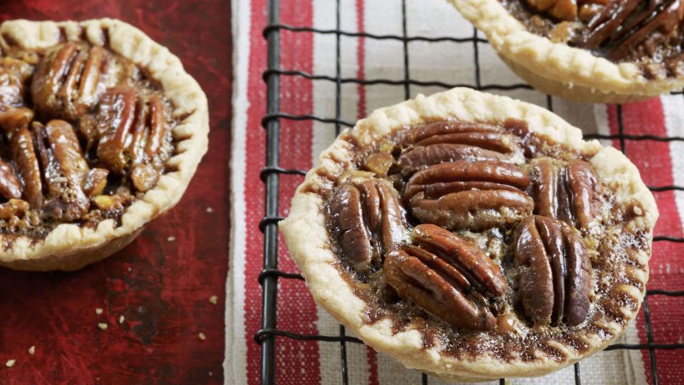 mini chocolate pecan tartlets on a wire rack over a red and white striped kitchen towel