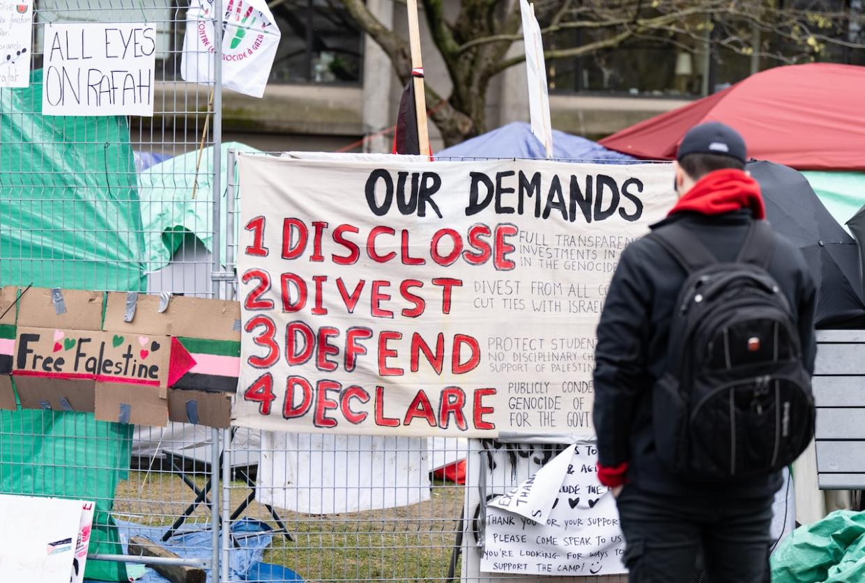 A man reads a sign of demands posted outside a pro-Palestinian encampment set up on McGill University's campus in Montreal on Tuesday.  (Christinne Muschi/The Canadian Press - image credit)