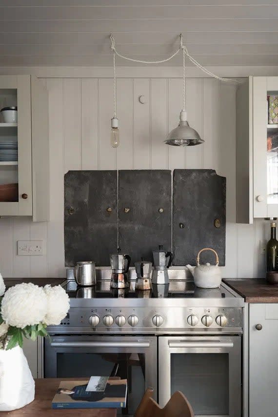 Stainless steel stove with lots of moka pots and coffee pots on top, kitchen painted in Purbeck Stone by Farrow & Ball.