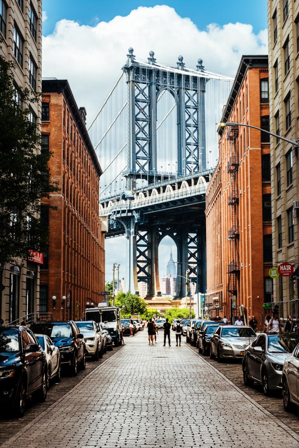 For who walk through the cobblestone street in Brooklyn’s Dumbo neighborhood, the sudden sight of Manhattan Bridge might come as a splendid surprise. At the intersection of Washington and Water Street, locals and tourists alike can take in the majestic beauty of the longest bridge connecting Manhattan and Brooklyn (the span bearing the moniker of the former is 866 feet longer than that named after the latter). Of course, making the view all the more dramatic are the symmetrical buildings on either side of Washington Street, creating one of the best architectural photograph opportunities in the borough.