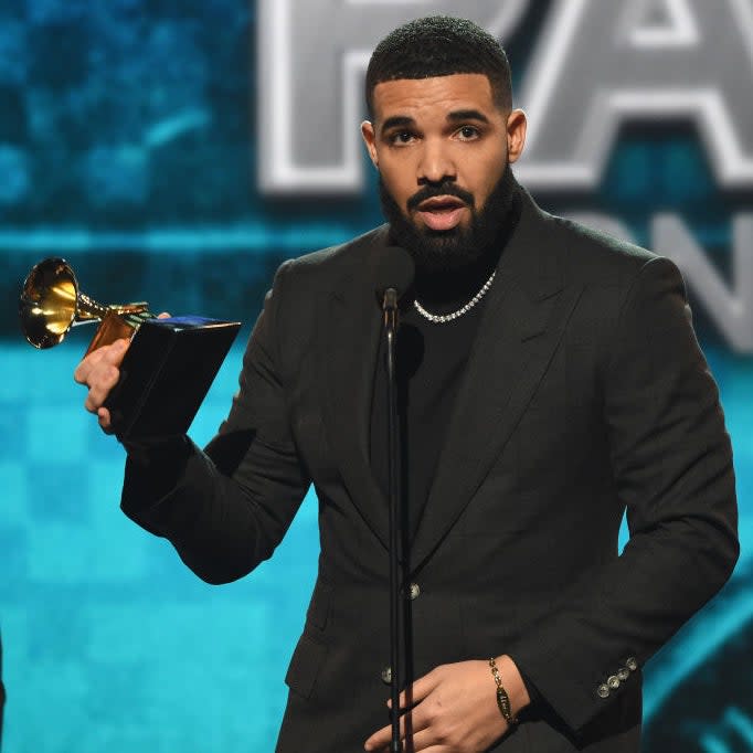 Drake in a formal suit holding a Grammy award on stage