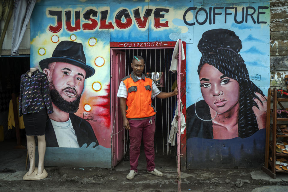 Gyslain, 39, poses in front of his hairdressing salon in Goma, Democratic Republic of Congo, Saturday Nov. 26, 2022.At a time of tension and economic uncertainty, the bold names and brightly colored storefronts bring a sense of normalcy to residents who have contended with conflict and natural disasters such as volcanic eruptions for decades. (AP Photo/Jerome Delay)