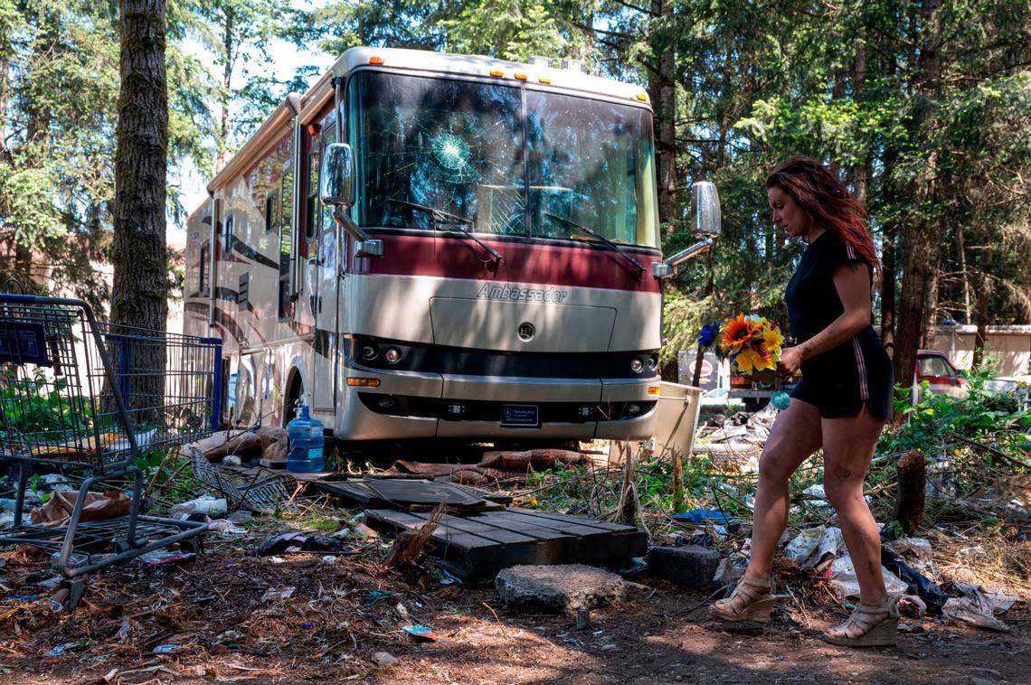 Kelsi Springs, 34, carries a bouquet of fake flowers that was given to her by a friend as she walks past a broken RV at a homeless encampment in the 9700 block of Steele Street South in Tacoma on Thursday, May 25, 2023.