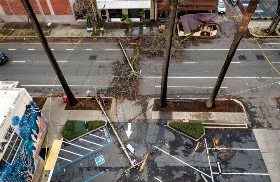 Two power poles rest on the ground in front of Bombay Bar and Grill – which saw its covered outdoor patio destroyed by the same storm – on 21st Street in midtown Sacramento on Wednesday. Police closed two blocks of the street because of downed power lines.