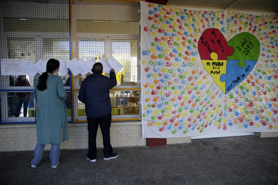 People check voting sections lists next to a banner celebrating World Autism Day with the words "My world is your world, at a polling station for Spain's general election in Madrid, Sunday, April 28, 2019. Galvanized by the Catalan crisis, Spain's far right is set to enter Parliament for the first time in decades while the Socialist government tries to cling on to power in Spain's third election in four years. (AP Photo/Andrea Comas)