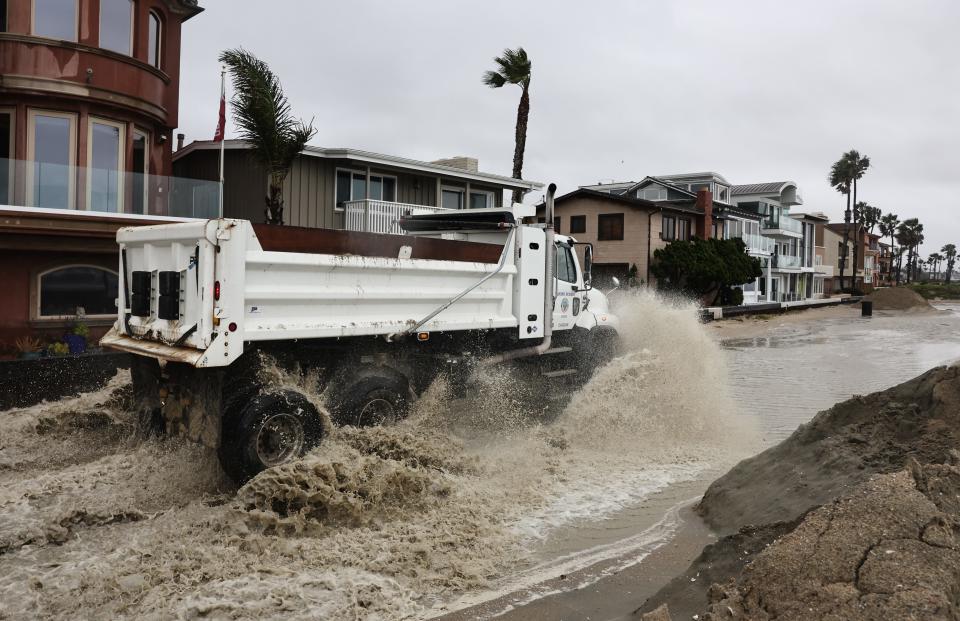 A truck drives through standing water while creating sand berms to protect beachfront homes from flooding on Wednesday, in Long Beach, Calif.