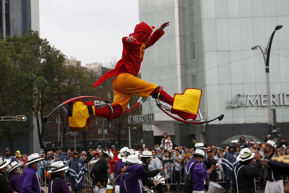 A performer dressed as Mexican pop culture super hero "El Chapulin Colorado" jumps into the air with the help of leg extensions during the Day of the Dead parade in Mexico City, Saturday, Nov. 2, 2019. (AP Photo/Ginnette Riquelme)