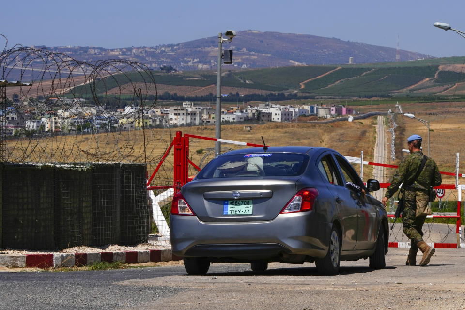 A U.N. Peacekeeper stops a car at a checkpoint on a road that leads to the outskirts of Ghajar in the background in the southern village of Majidiyeh, Lebanon, Tuesday, July 11, 2023. The little village of Ghajar has been a point of contention between Israel and Lebanon for years, split in two by the border between Lebanon and the Israeli-occupied Golan Heights. The dispute has begun to heat up again.(AP Photo/Hassan Ammar)