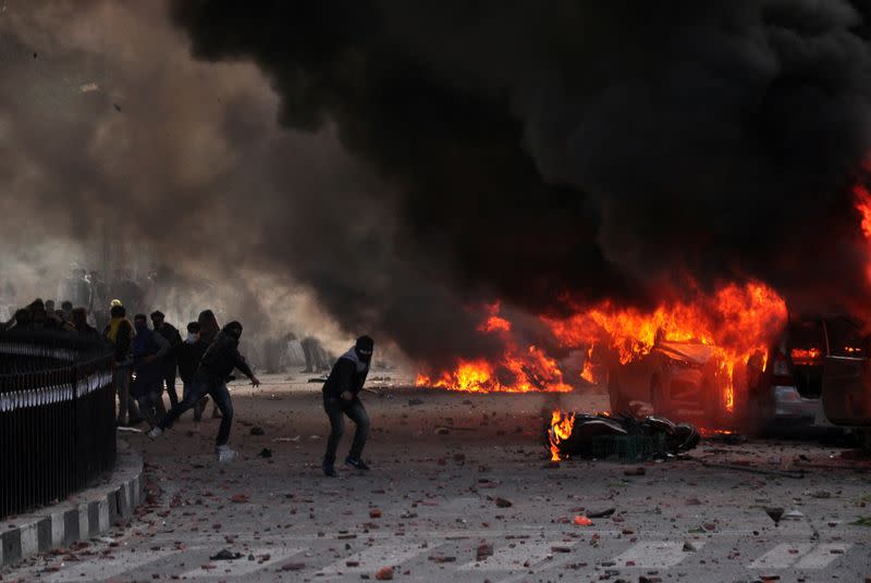Demonstrators throw stones towards police next to burning vehicles during a protest against a new citizenship law, in Lucknow
