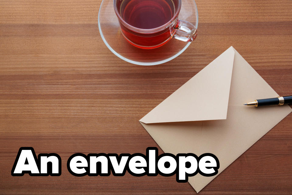 A cup of tea sits next to a sealed envelope with a pen on a wooden table