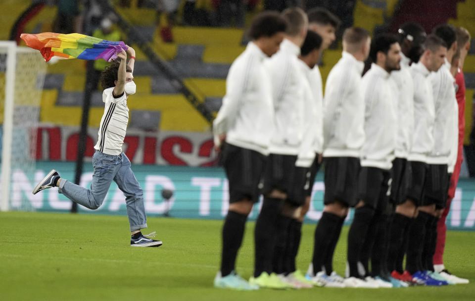 A fan with a LGBT pride flag runs on the pitch during the national anthems before the Euro 2020 soccer championship group F match between Germany and Hungary at the Allianz Arena in Munich, Germany, Wednesday, June 23, 2021. (AP Photo/Matthias Schrader, Pool)