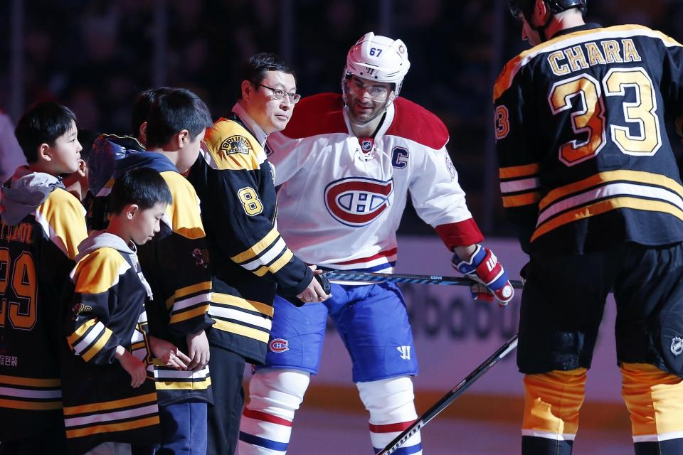 FILE - In this Feb. 12, 2017, file photo, ORG Packaging Chairman Zhou Yunjie (8) prepares for the ceremonial puck drop with Boston Bruins' Zdeno Chara (33), of Slovakia, and Montreal Canadiens' Max Pacioretty (67) before an NHL hockey game in Boston. While being awarded the Olympics was impetus for the Chinese government to pour resources into hockey, it’s getting some help from the private sector in the form of ORG Packaging chairman Zhou Yunjie. Known as “Mr. Zhou,” the goaltender-turned-billionaire is at the forefront of hockey’s growth in China through NHL partnerships and sponsorships and hopes the league can be as successful as the NBA in his country.(AP Photo/Michael Dwyer, File)