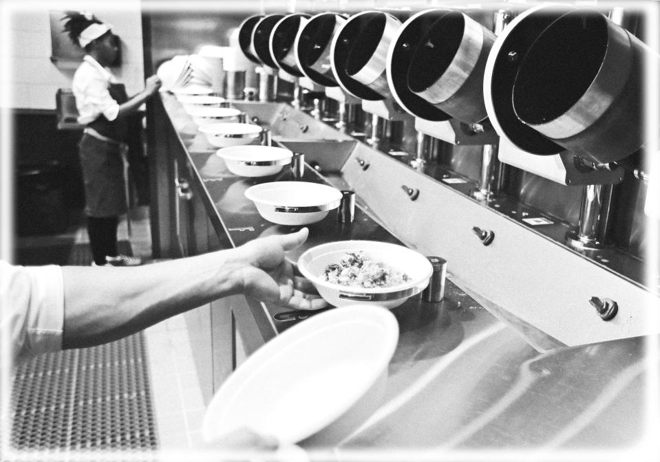 A worker lifts a lunch bowl off the production line at Spyce, a restaurant which uses a robotic cooking process, in Boston. (Photo: Charles Krupa/AP, digitally enhanced by Yahoo News)