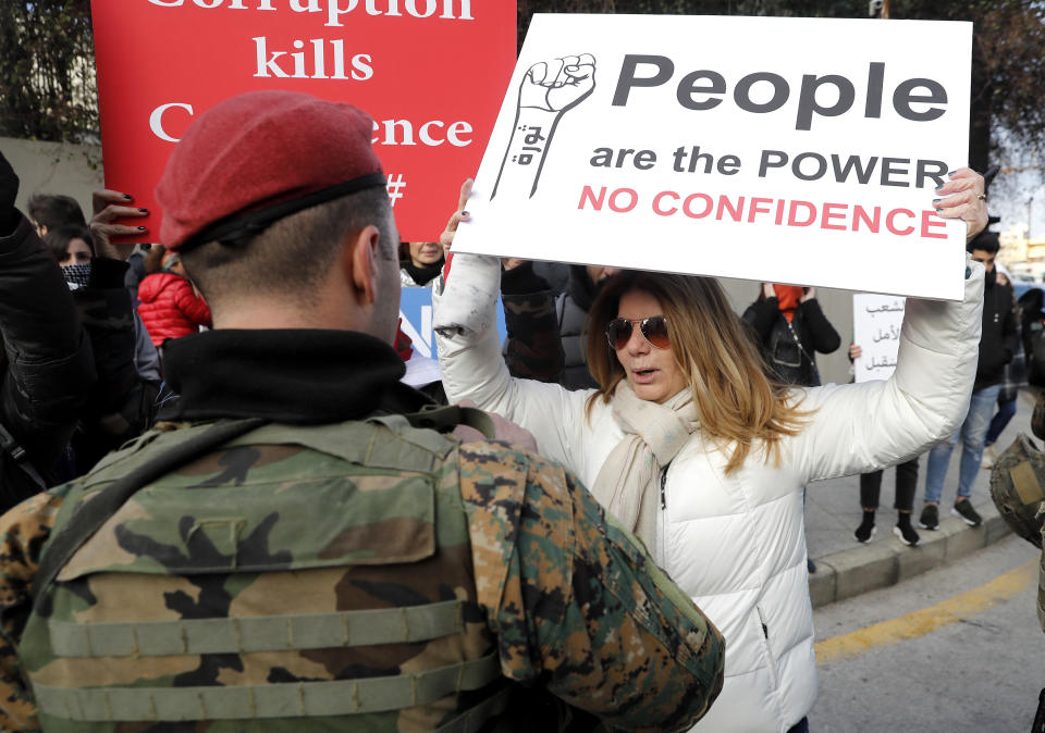 A protester holds a placard denouncing the government in front of soldiers during a protest against a parliament session to vote of confidence for the new government, in downtown Beirut, Lebanon, Tuesday, Feb. 11, 2020. (AP Photo/Hussein Malla)