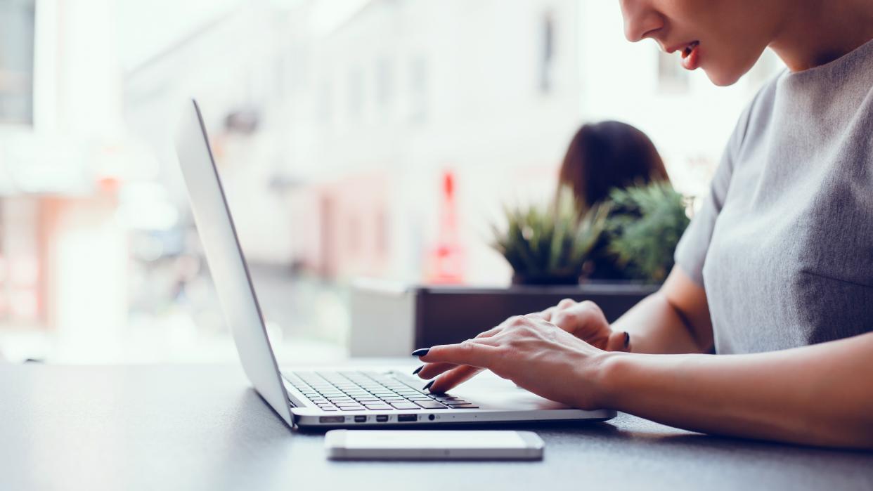  A woman sitting at a table, working on a MacBook laptop. 