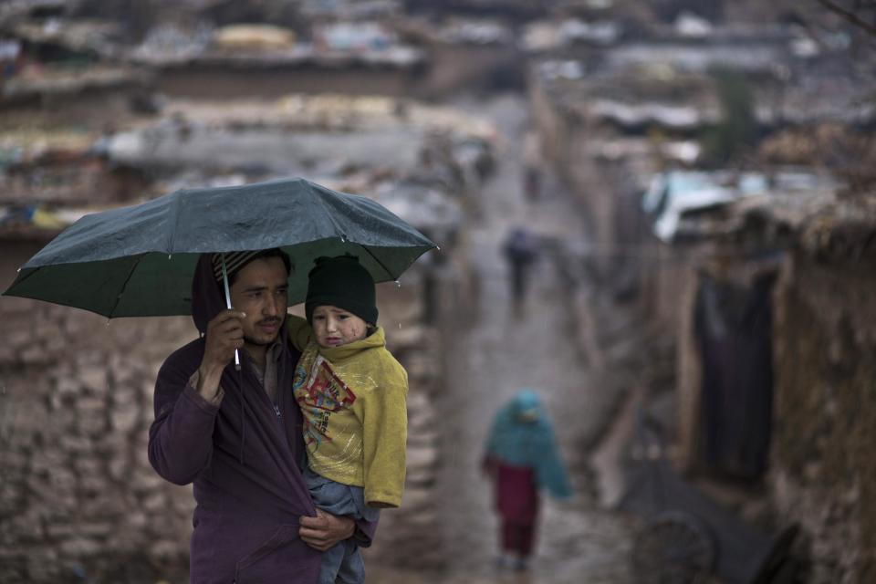 A Pakistani man, who was displaced from Pakistan's tribal areas due to fighting between the Taliban and the army, holds an umbrella to shelter his son and himself from the rain while walking toward the main way from a poor, on the outskirts of Islamabad, Pakistan, Thursday, Feb. 6, 2014. (AP Photo/Muhammed Muheisen)